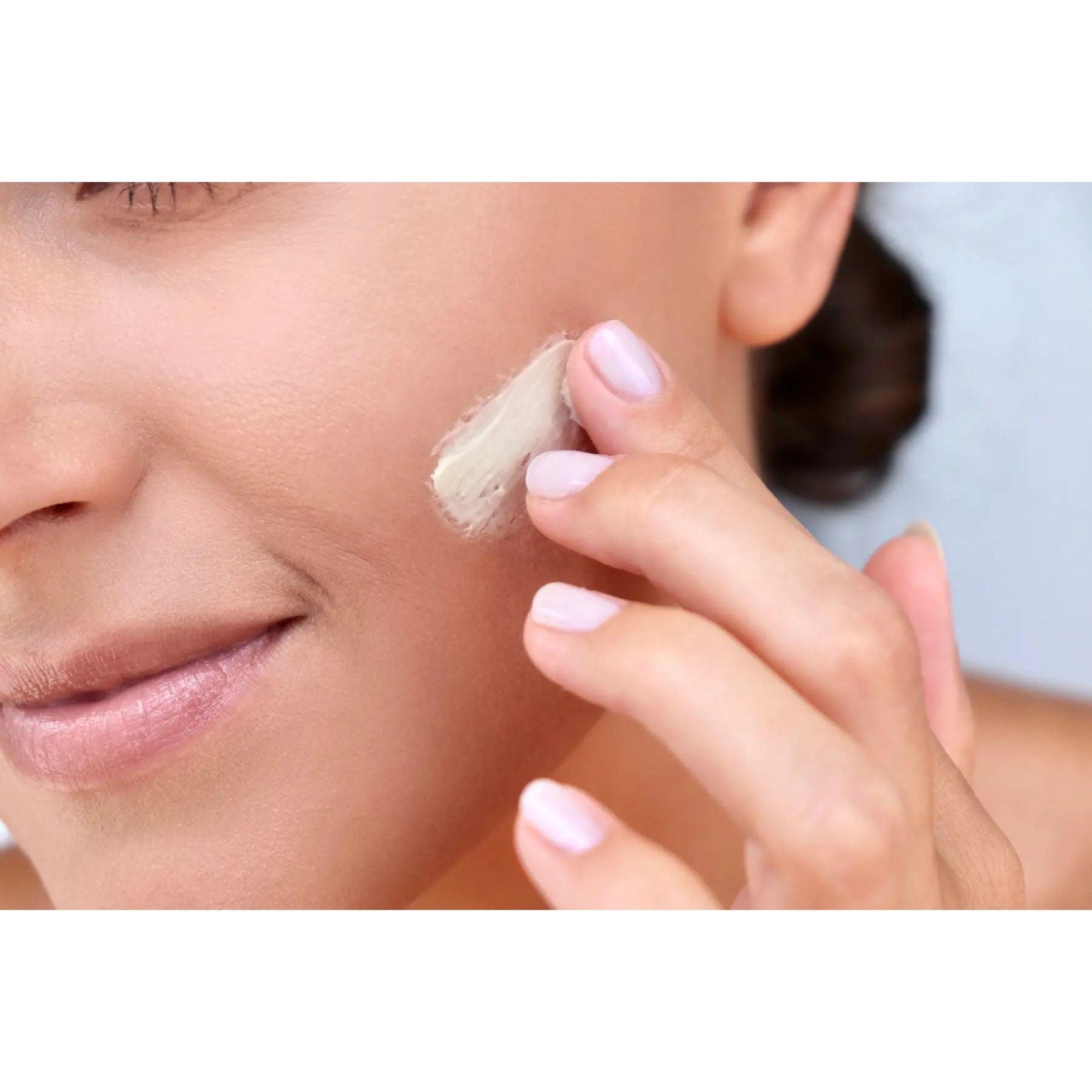 Woman applying a rich crème to her face, showcasing hydrating skincare routine for a luminous complexion.