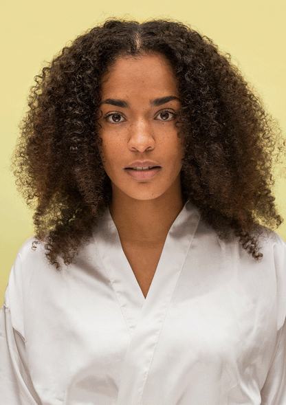 Model with natural curls wearing a silk robe against a light background, showcasing the beauty of defined, bouncy curls.