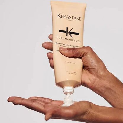 Hand dispensing Kérastase Curl Manifesto Fondant Hydration Essentielle, a moisturizing conditioner for curly hair.