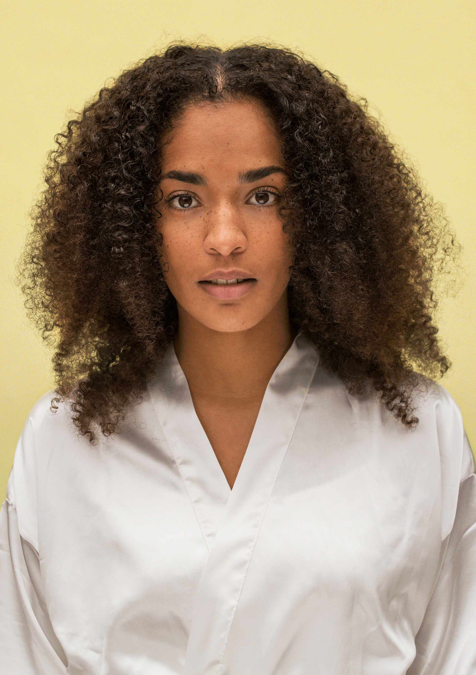 Model showcasing healthy curls wearing a silk robe against a yellow background, emphasizing natural hair beauty.
