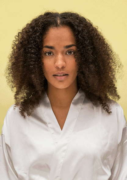 Model showcasing healthy curls wearing a silk robe against a yellow background, emphasizing natural hair beauty.