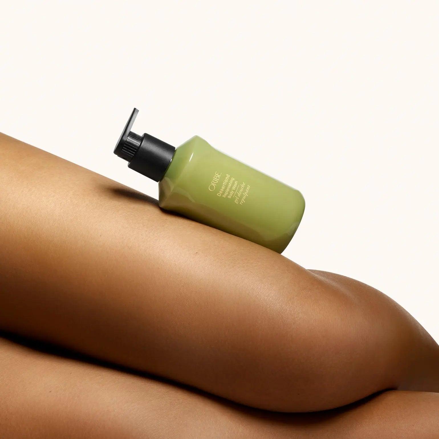 Oribe Desertland Replenishing Body Wash bottle resting on smooth skin, showcasing luxurious cleansing and hydration benefits.