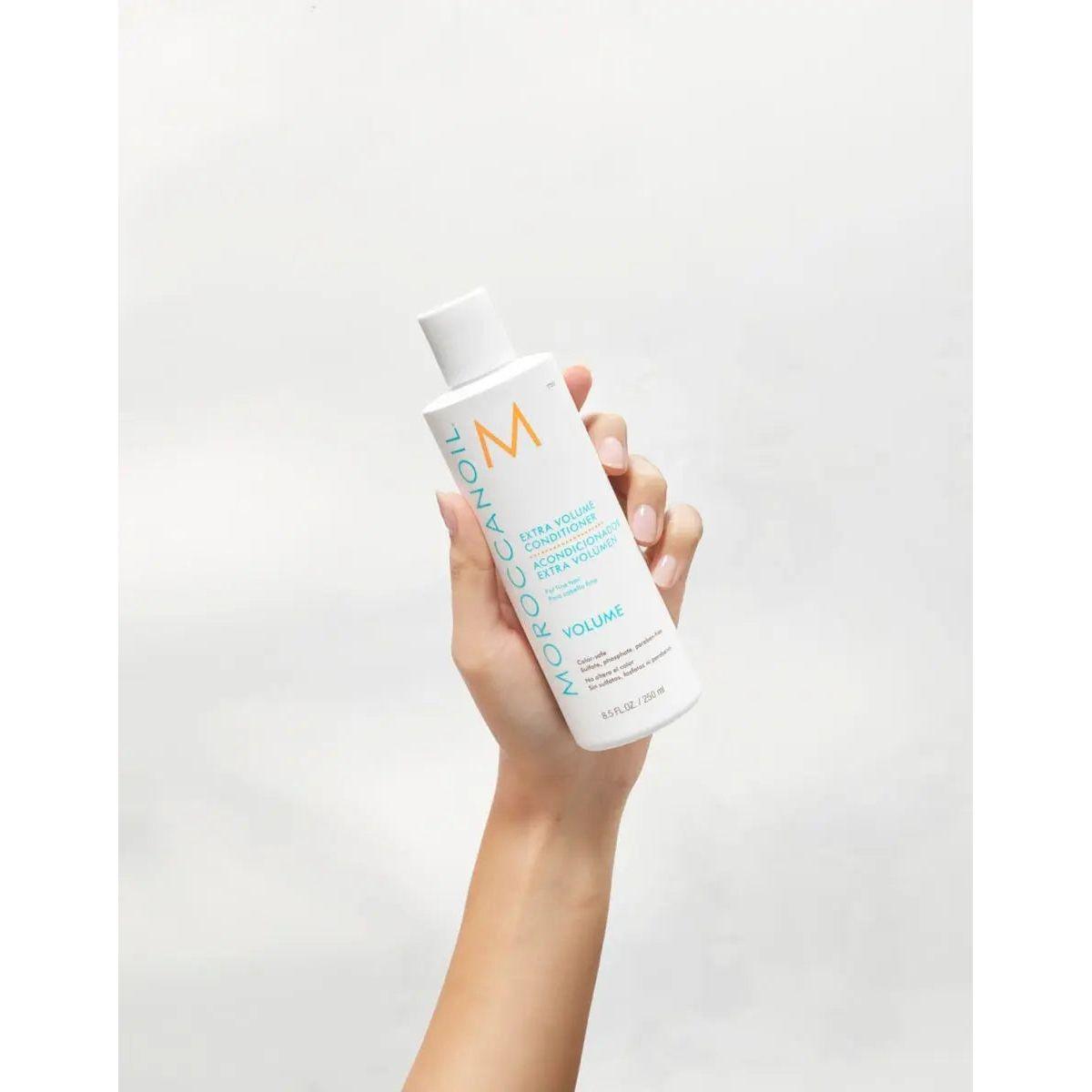 Moroccanoil Extra Volume Conditioner bottle held in hand, showcasing its lightweight formula for fine hair volume.