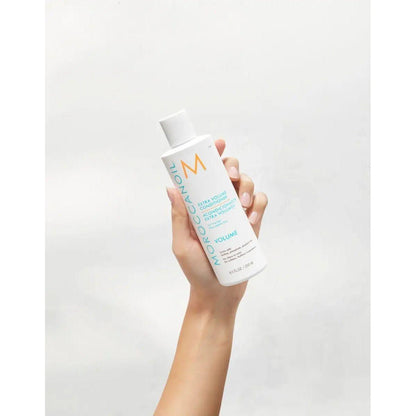 Moroccanoil Extra Volume Conditioner bottle held in hand, showcasing its lightweight formula for fine hair volume.