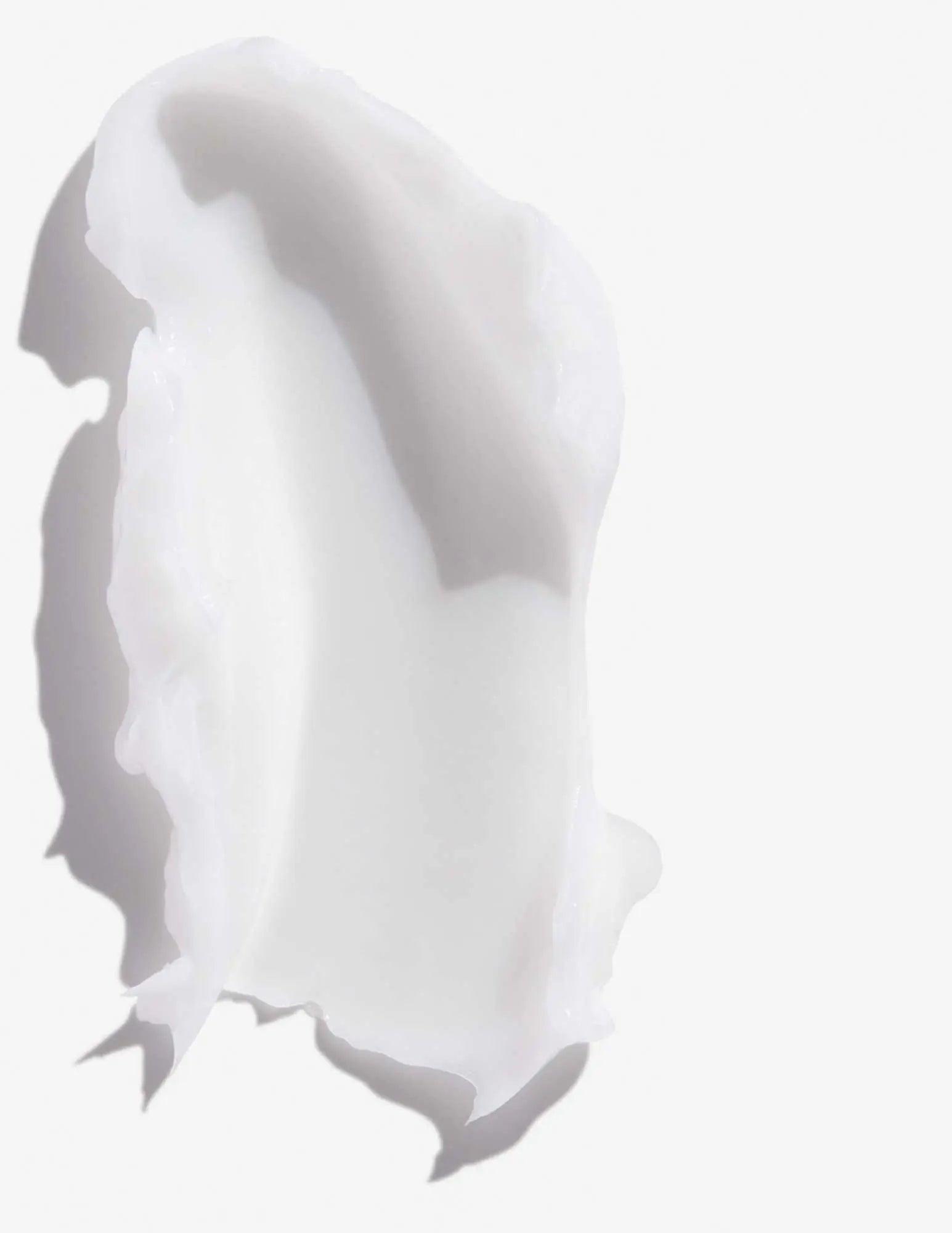 Creamy texture of Redken Frizz Dismiss Conditioner on a white background for frizz control and hair smoothness.