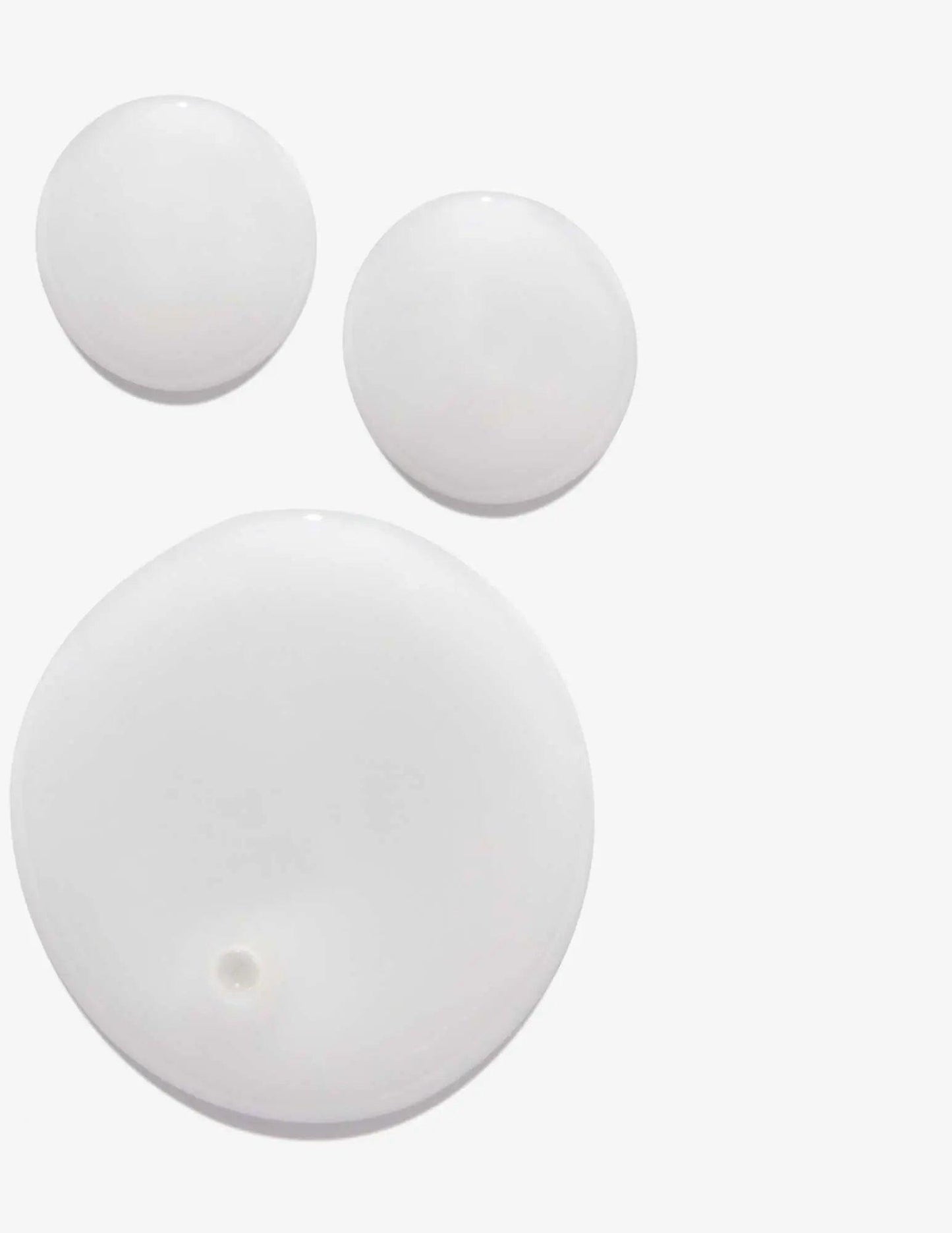 Three white circular drops of shampoo on a clean background, showcasing a lightweight and smooth texture.