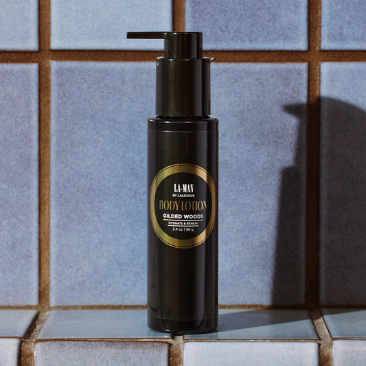 Gilded Woods Body Lotion in a sleek pump bottle against blue tiled background, offering hydration and nourishment for skin.