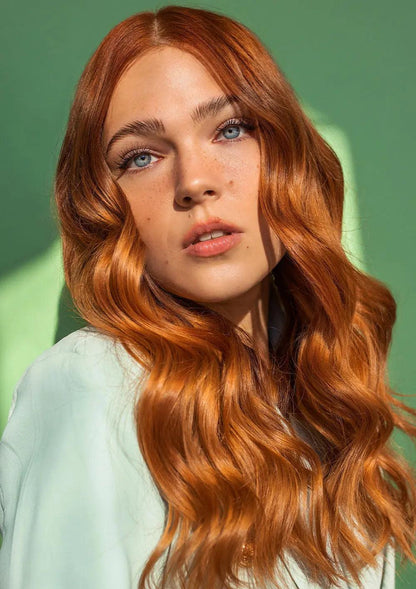Model with shiny, wavy red hair showcasing healthy locks against a green background.