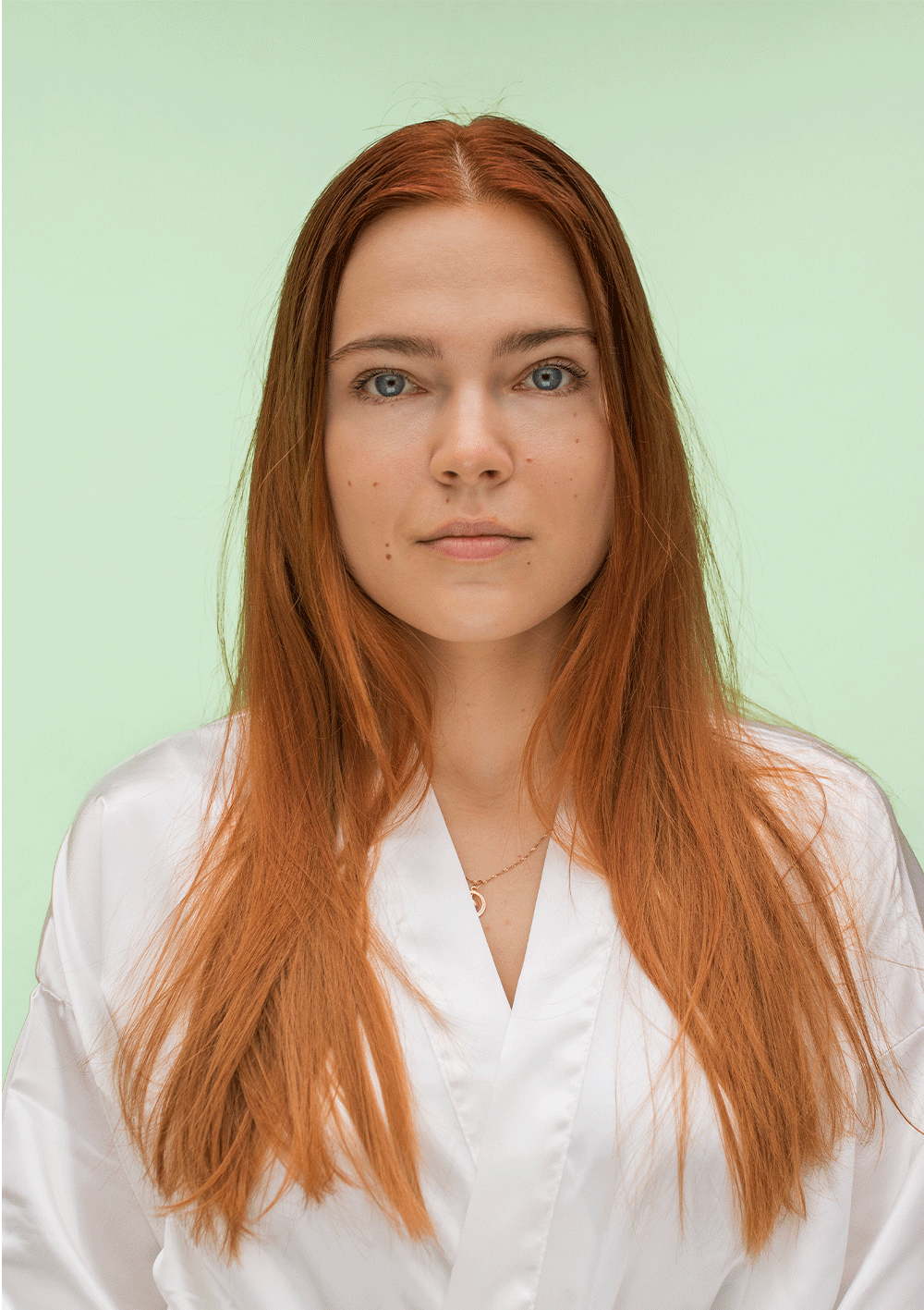 Model with long red hair wearing a white robe against a light green background, showcasing healthy hair.