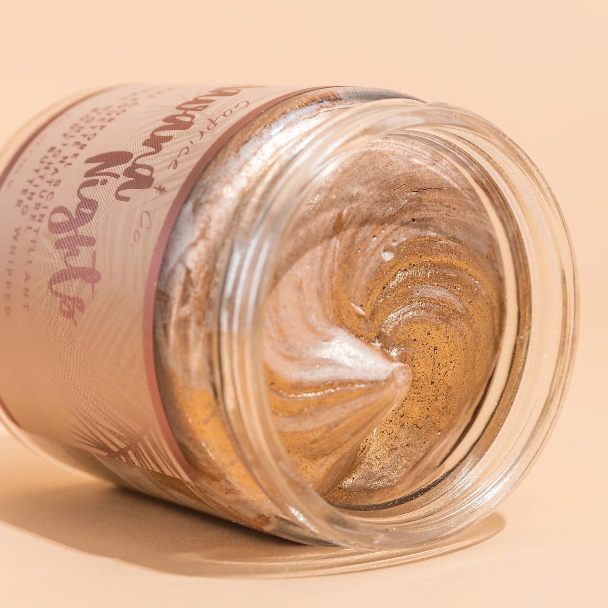 Shimmering bronze body butter in jar, showcasing creamy texture and luxurious golden swirls. Perfect for summer glow.