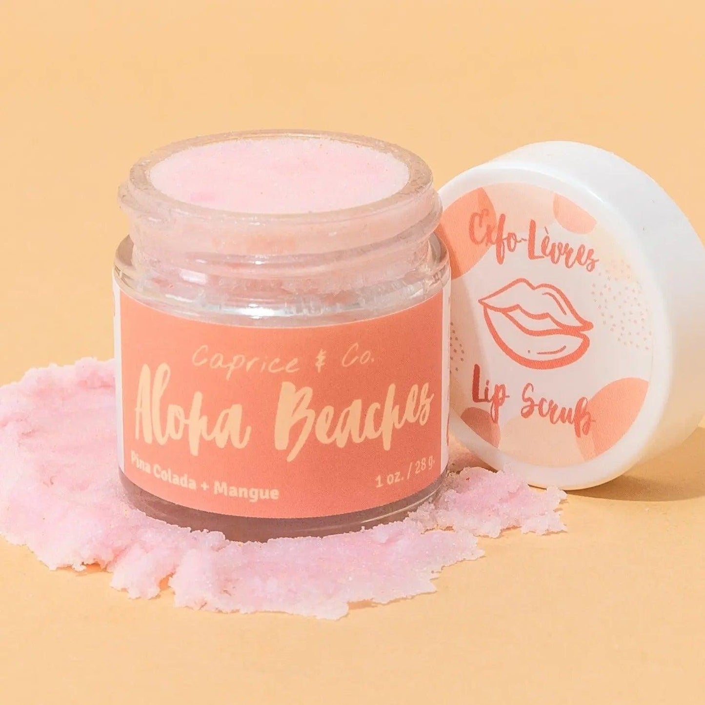 Lip scrub jar labeled "Aloha Beaches" with Pina Colada flavor, on a peach background, showcasing pink sugar exfoliant.
