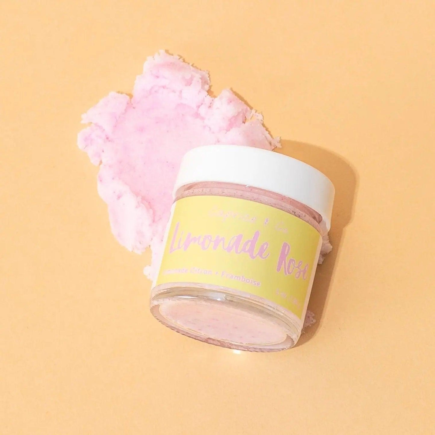 Lip Scrub Limonade Rose in a jar, with a pink sugar scrub piece, set against a light orange background.