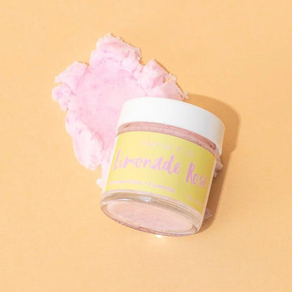 Lip Scrub Limonade Rose in a jar, with a pink sugar scrub piece, set against a light orange background.