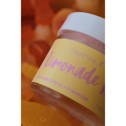 Lip scrub jar labeled "Limonade Rose" with a lemon and raspberry flavor against a colorful fruit background.