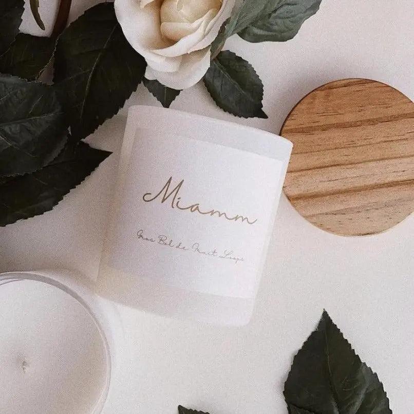 Miamm Fruit Loops candle in a reusable glass jar with wooden lid, surrounded by leaves and a rose.