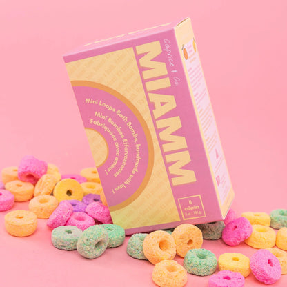 Miamm mini bath bombs packaging surrounded by colorful bath bomb rings on a pink background.