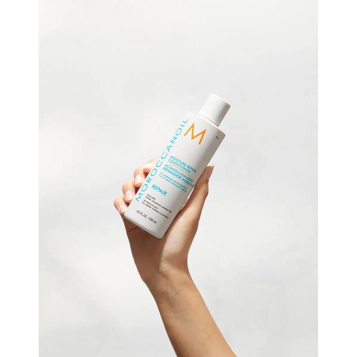 Moroccanoil Moisture Repair Conditioner held in a hand, designed to hydrate and restore damaged hair.