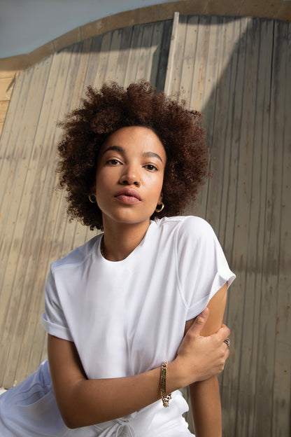 Model with curly hair wearing a white shirt, posing against a wooden background in natural light.
