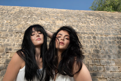 Two women showcasing voluminous, shiny hair styled with Neu Styling Mousse against a textured stone background.