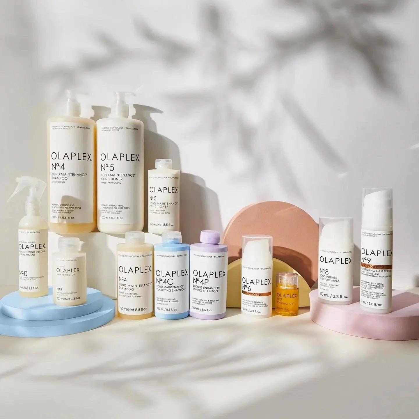 Collection of Olaplex hair care products including Nº.4 and Nº.5 Bond Maintenance Conditioner, displayed on colorful platforms.