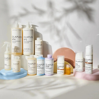 Collection of Olaplex hair care products including Nº.4 and Nº.5 Bond Maintenance Conditioner, displayed on colorful platforms.