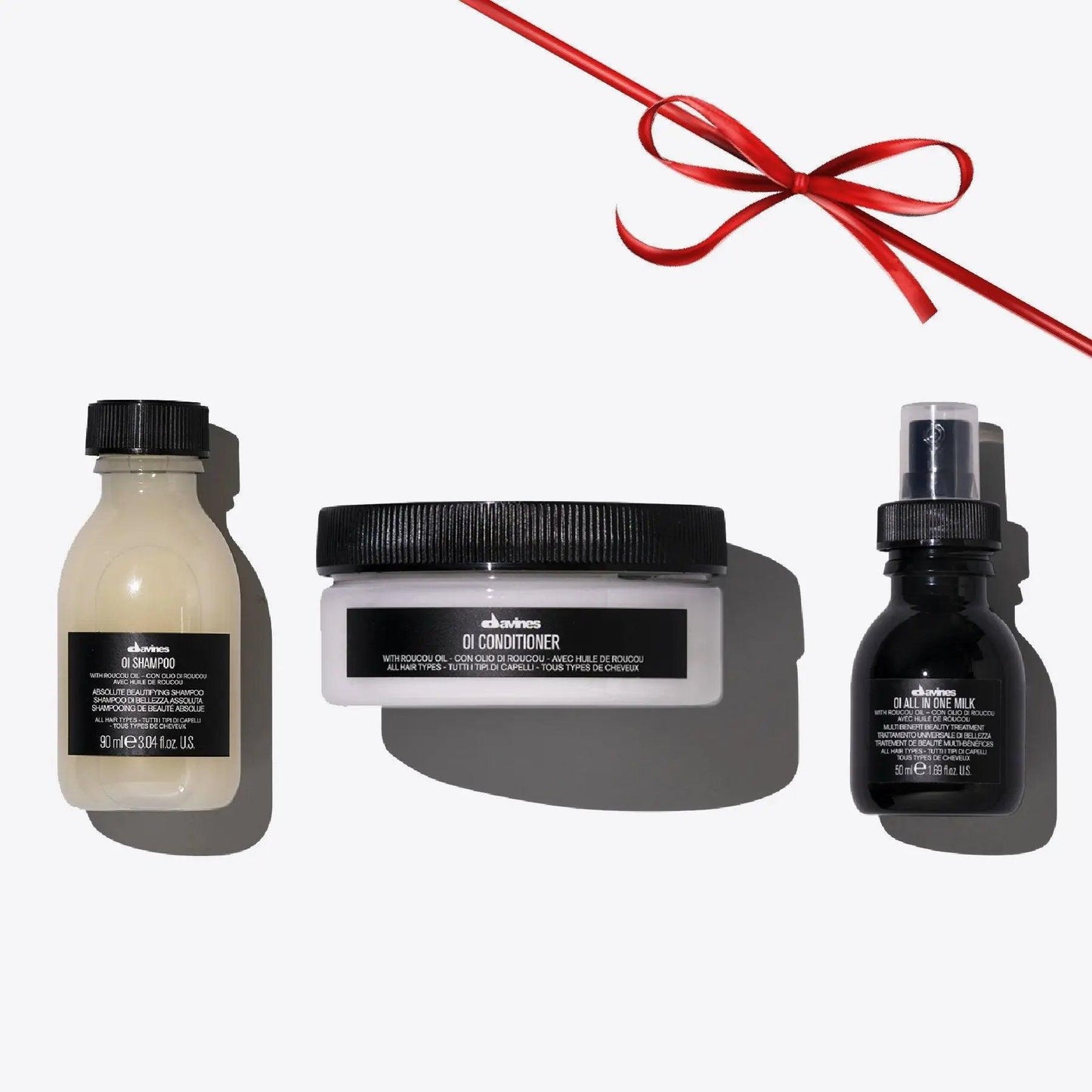 OI Travel Set with OI Shampoo, OI Conditioner, and OI All in One Milk on a white background with a red ribbon.