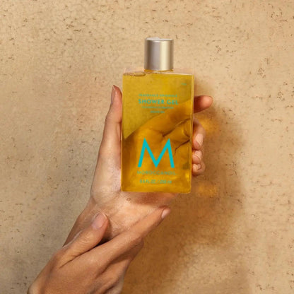 Person holding a bottle of Original Scented Shower Gel infused with argan oil against a textured background.