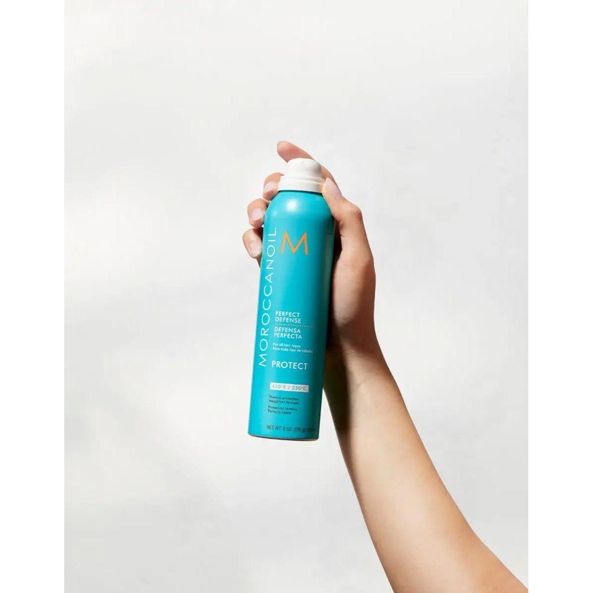 Hand holding Moroccanoil Perfect Defense Heat Protectant spray, showcasing argan oil-infused hair protection.