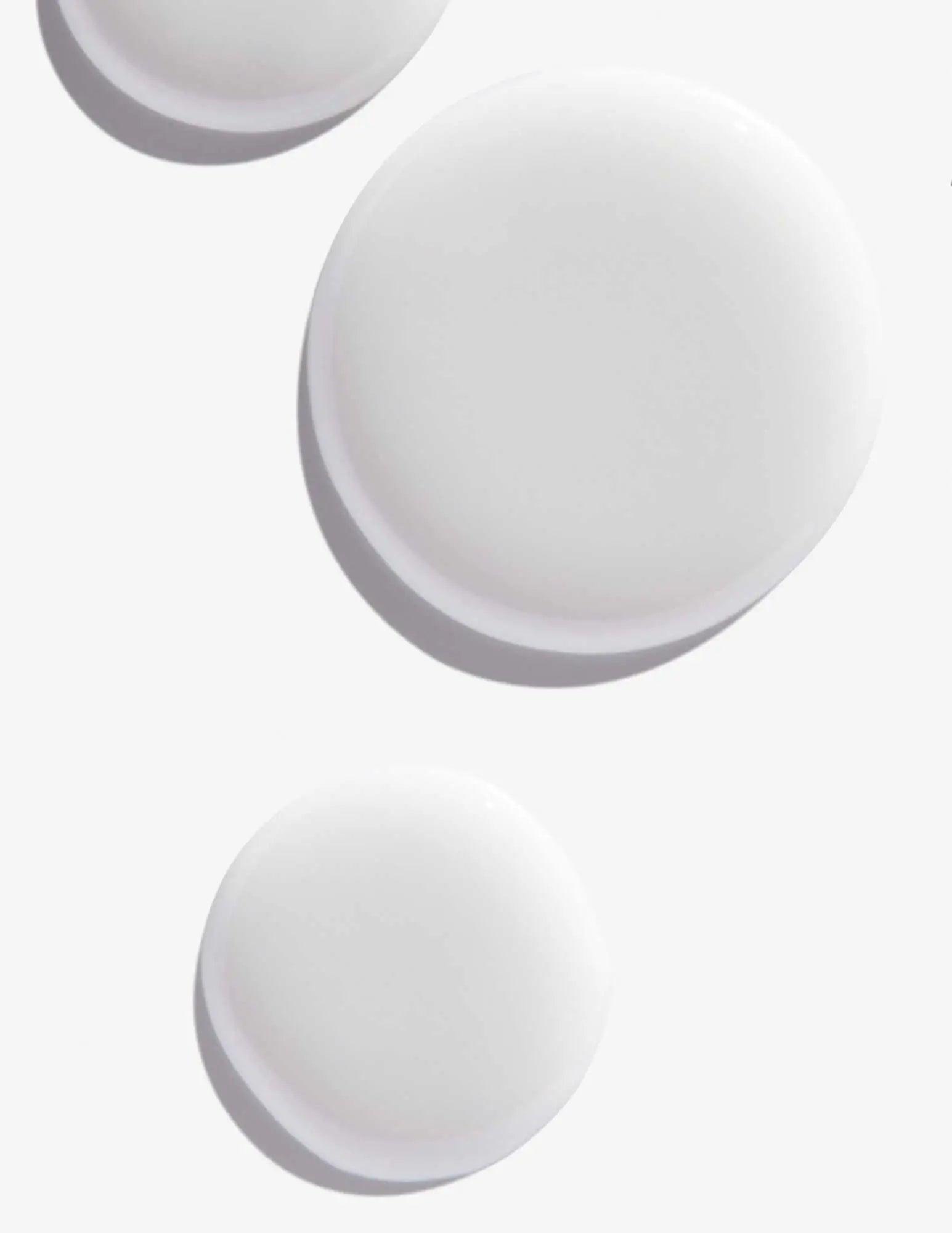 White round droplets of Scalp Relief Dandruff Shampoo on a light background, showcasing its smooth texture.