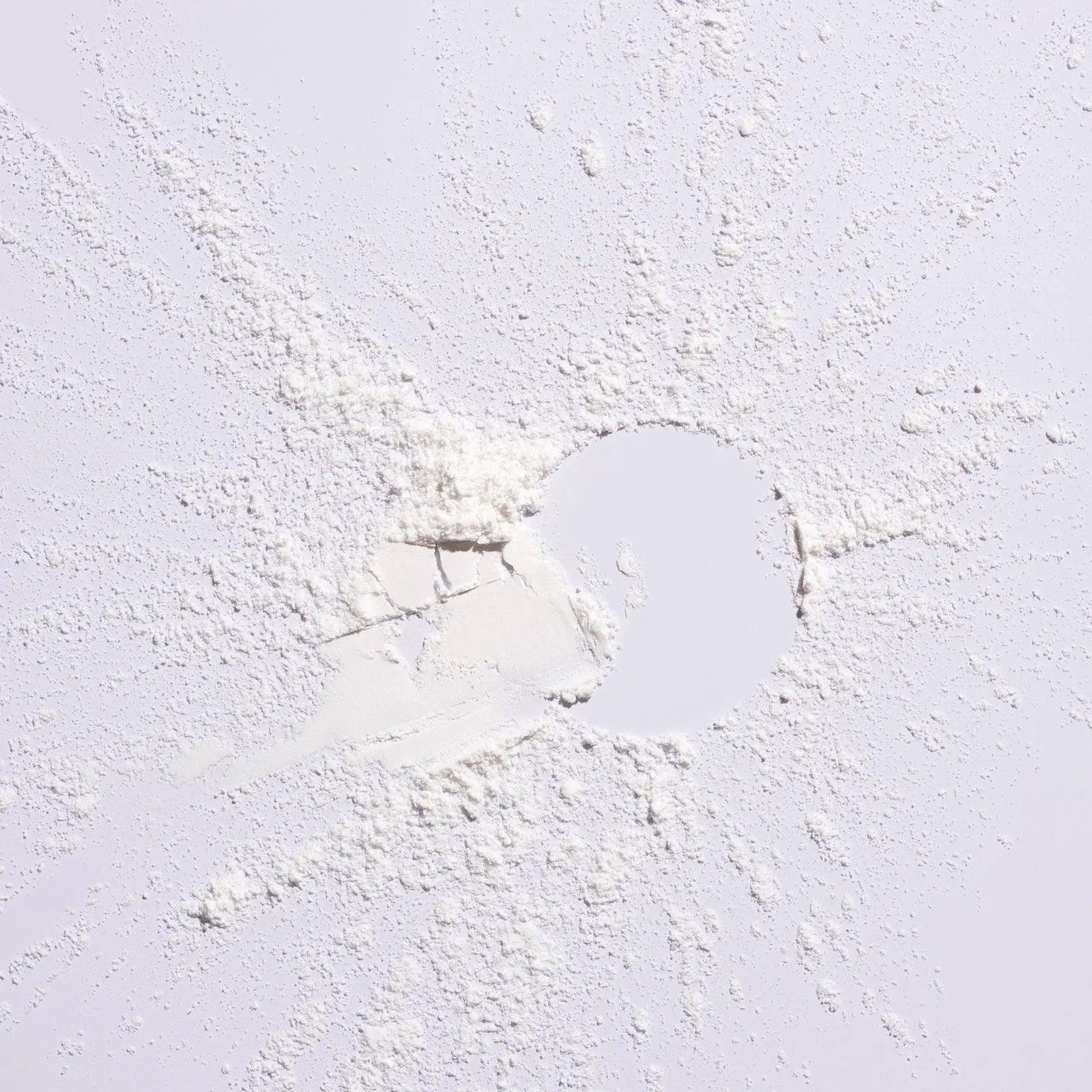 White powder scattered on a surface, representing Serene Scalp Oil Control Dry Shampoo Powder by Shu Uemura.