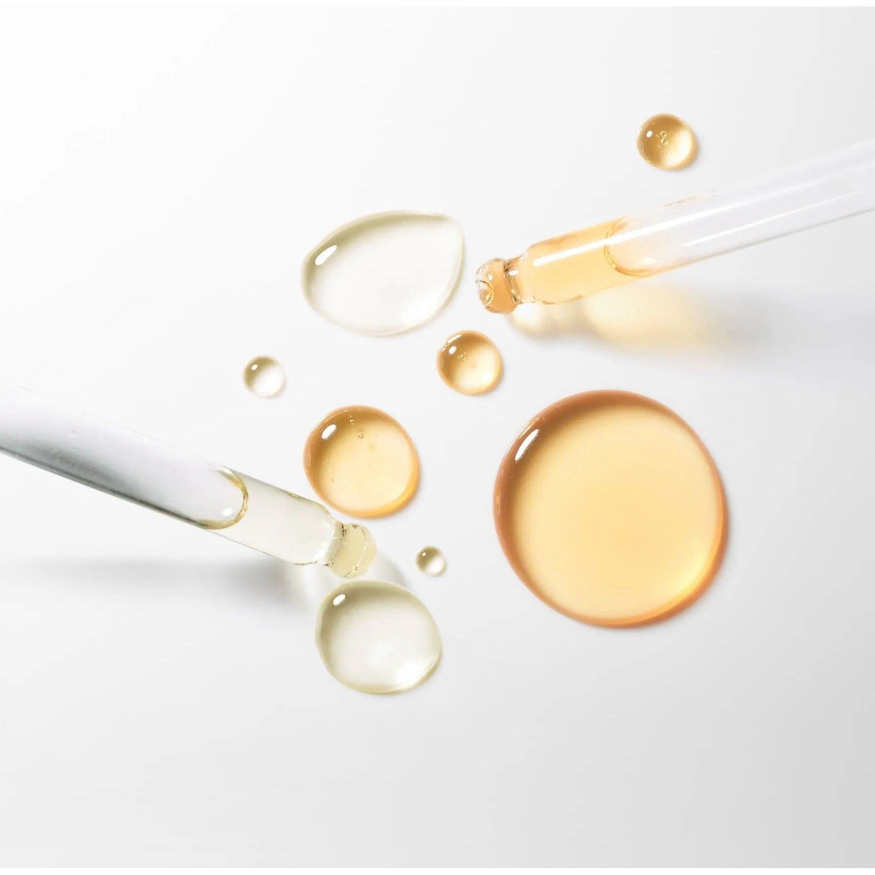 Close-up of facial serum drops and pipettes on white background showing beauty oil texture for skincare routine.