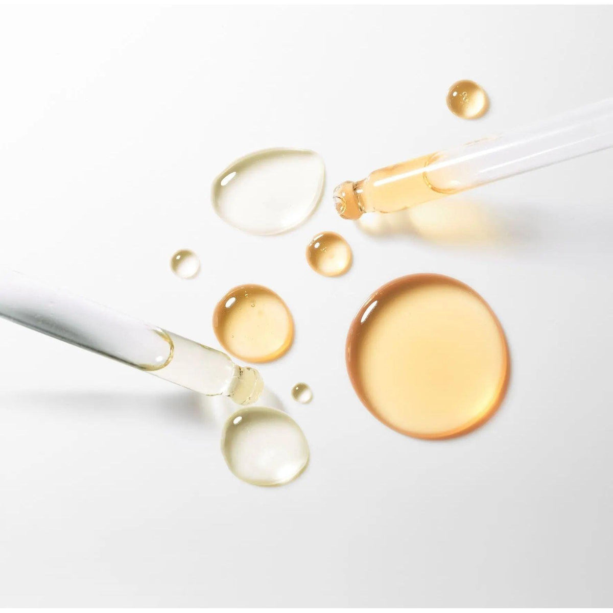 Close-up of facial serum drops and pipettes on white background showing beauty oil texture for skincare routine.