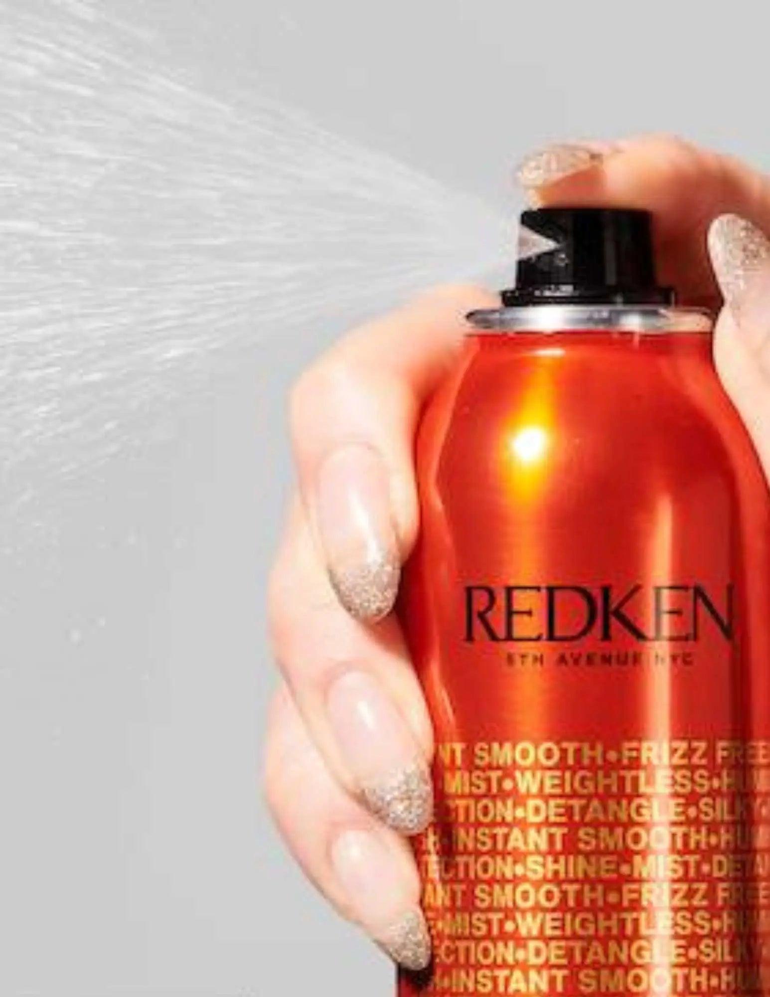 A hand holding a Redken Spray Smooth can, releasing a fine mist to control frizz and enhance hair manageability.