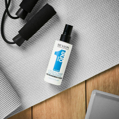 Revlon Uniq One Lotus Flower Hair Treatment bottle on gray yoga mat with dumbbell and fitness equipment.