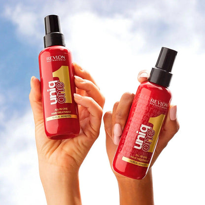 Revlon Professional Uniq One all-in-one hair treatment bottle held by two hands against a blue sky background.
