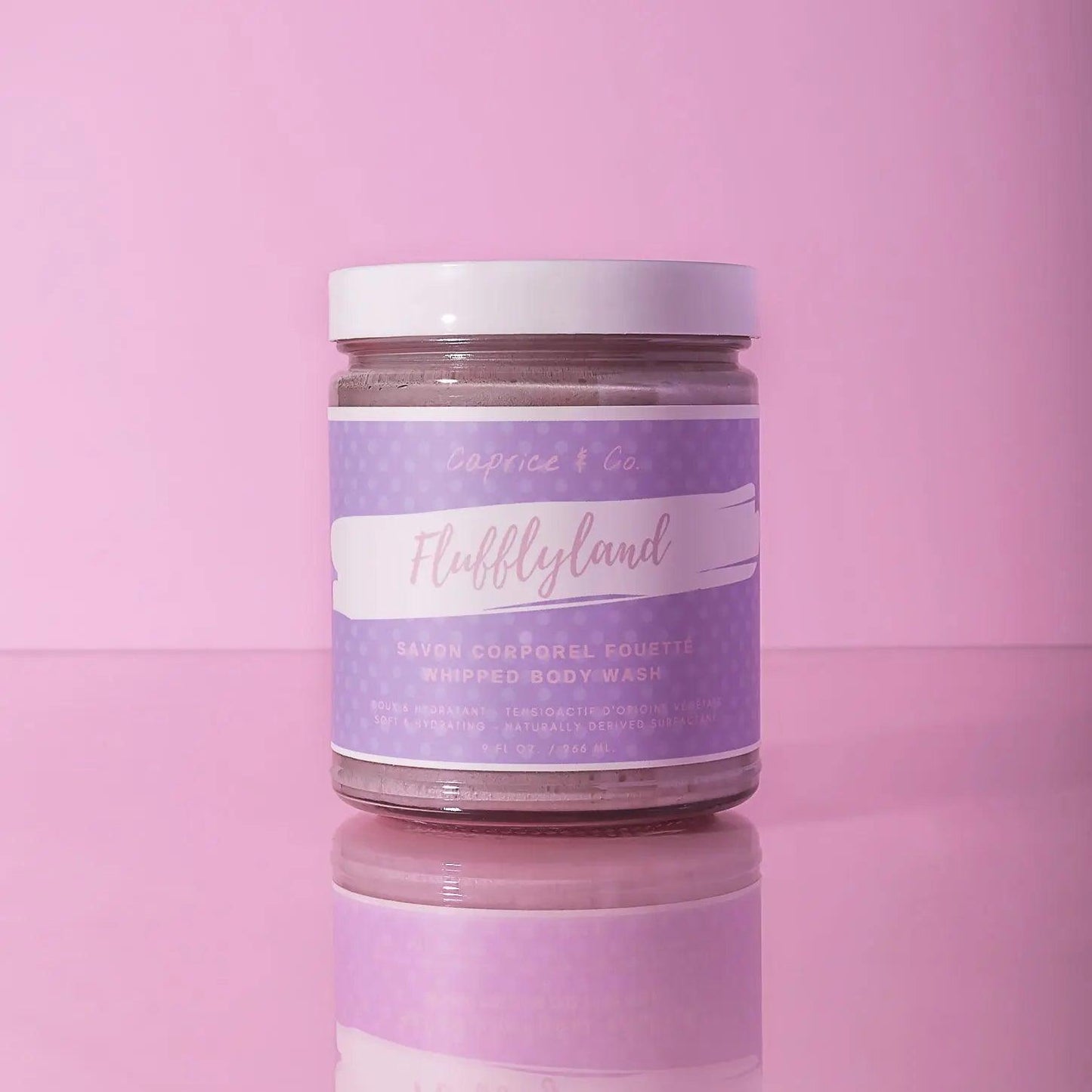Fluffyland whipped body wash in a clear jar with lavender label on pink background, perfect for moisturizing skin.